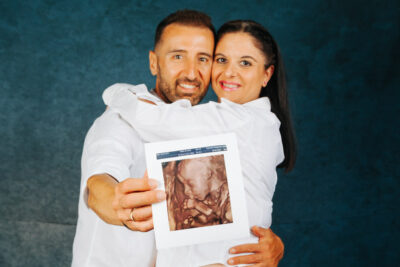ζευγάρι άνδρας γυναίκα, αγκαλιά χαμογελαστοί στο φακό η γυναίκα είναι έγκυος κρατούν έναν υπέρηχο